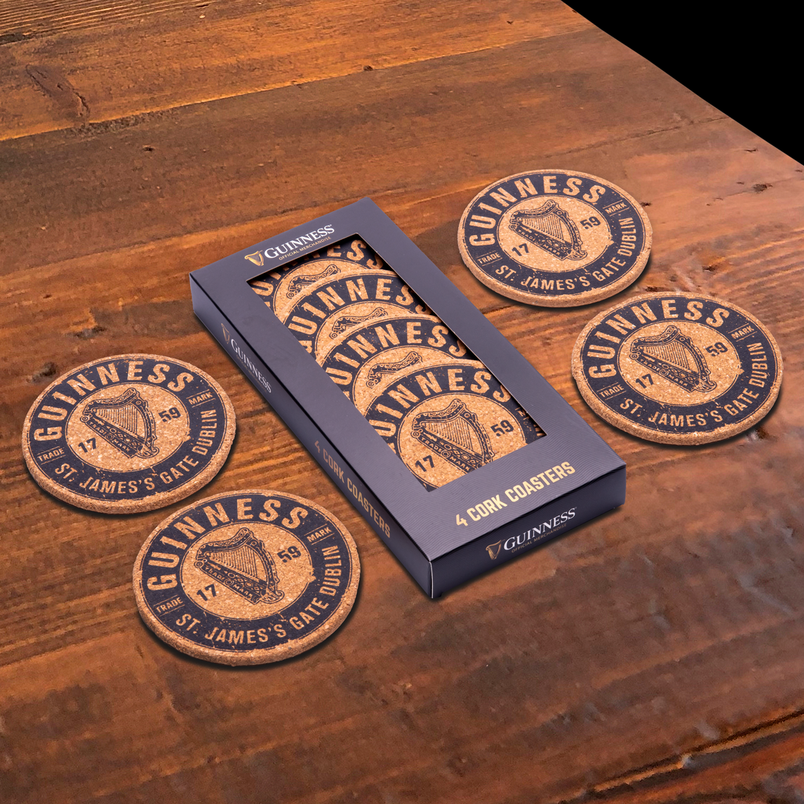 The Guinness Cork Coaster Set - 4 PK from Guinness Official Merchandise is showcased on a wooden surface, with each of the four coasters beautifully displaying the iconic Guinness Harp and accompanied by its packaging.