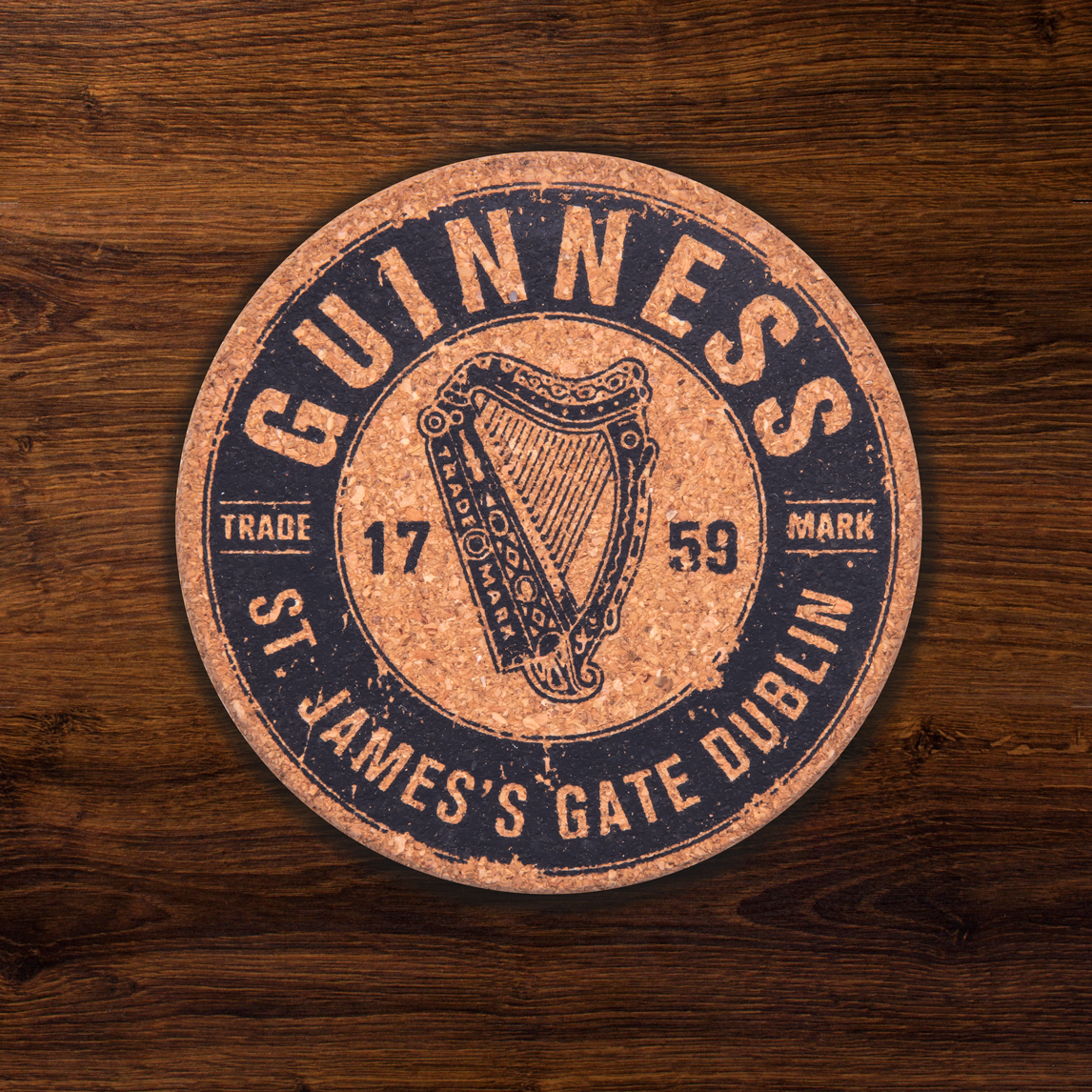 A monochrome round coaster from the Guinness Cork Coaster Set - 4 PK features the iconic harp, "St. James's Gate Dublin," and "Trade Mark 1759," elegantly displayed on a wooden surface.