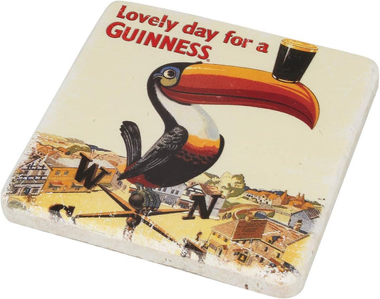 The Guinness Gilroy Toucan Stone Coaster features the iconic toucan balancing a pint above "Lovely day for a GUINNESS" and a charming town illustration. By Guinness.