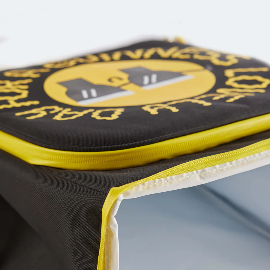 A close-up of the Guinness x Fatti Burke Sun Cooler Bag from Guinness Webstore UK, a black insulated lunch bag with a yellow zipper, featuring a graphic design inspired by Kathi Burke on the top flap.