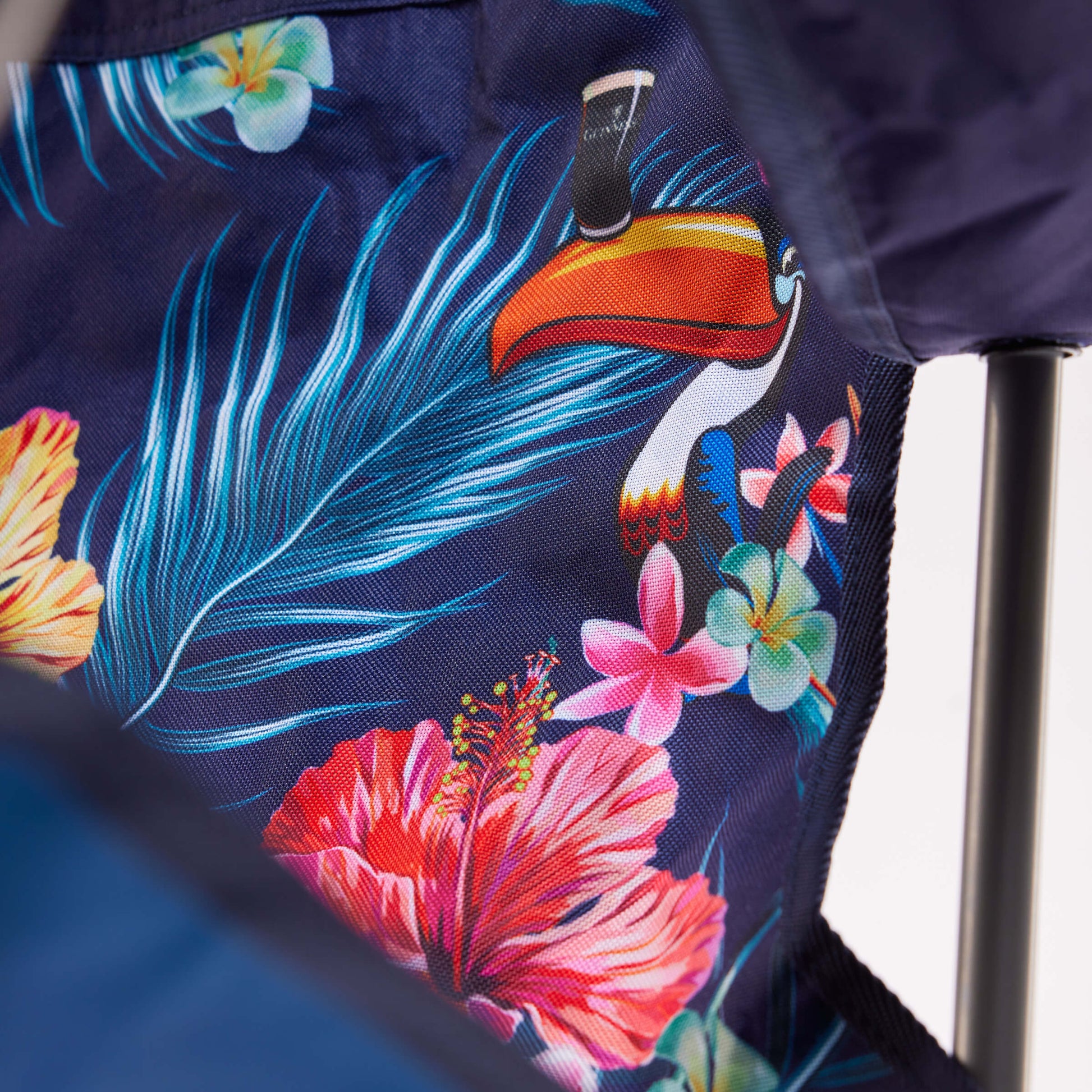 Close-up of fabric with tropical toucan, pink hibiscus flowers, and green palm leaves on dark blue—an ideal match for the Guinness Toucan Hawaiian Beach Chair from Guinness Webstore US or any beach essentials collection.