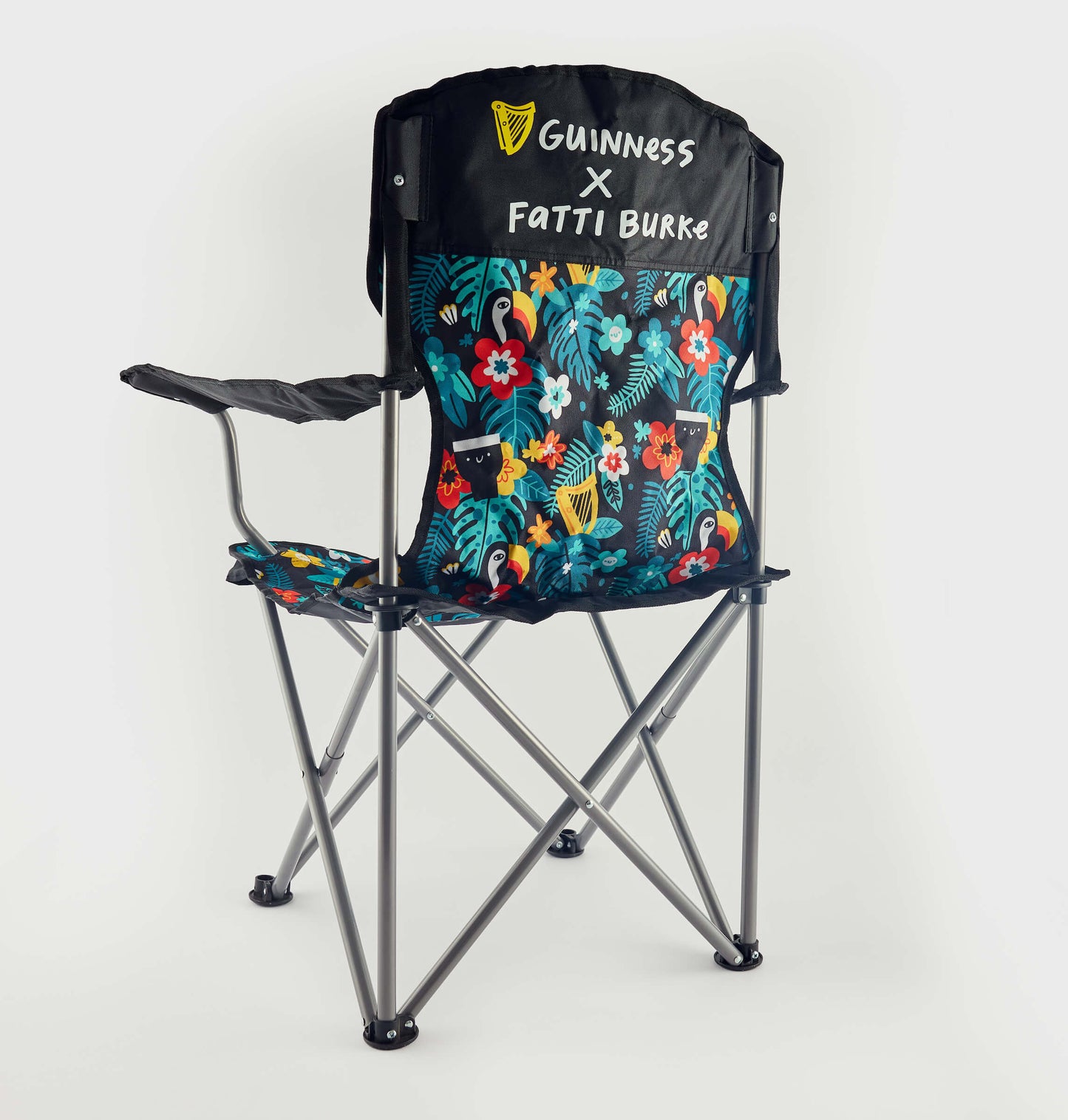 The Guinness x Fatti Burke Hawaiian Camping Chair features a sturdy metal frame, black armrests, and a vibrant floral pattern. "Guinness X Fatti Burke" appears in white on the backrest, evoking the look of a Hawaiian beach towel.