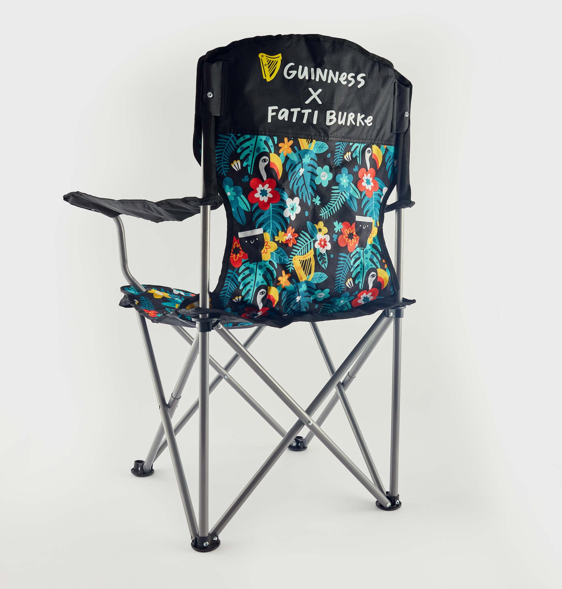 The Guinness x Fatti Burke Hawaiian Camping Chair features a sturdy metal frame, black armrests, and a vibrant floral pattern. "Guinness X Fatti Burke" appears in white on the backrest, evoking the look of a Hawaiian beach towel.