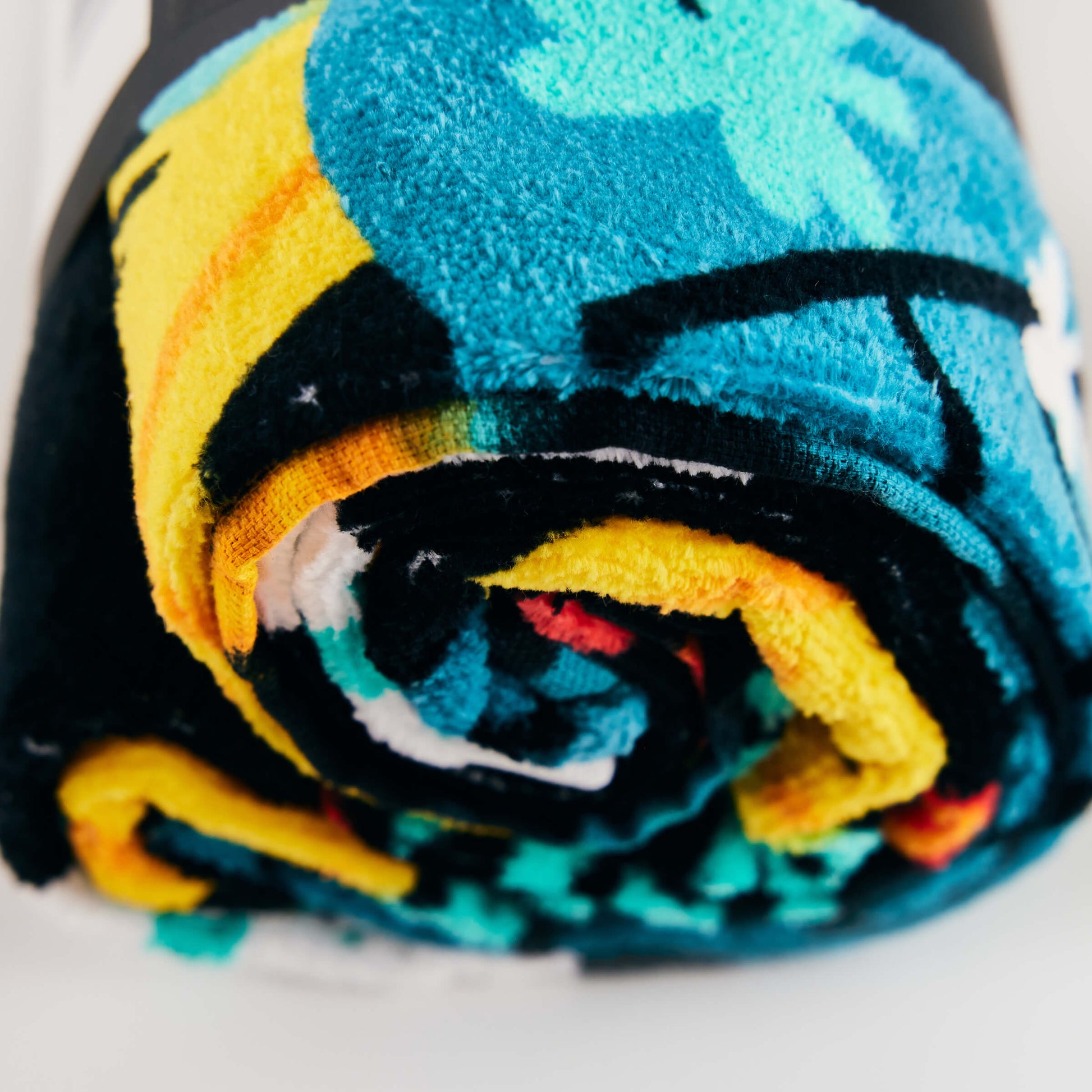 A close-up of the rolled-up Guinness x Fatti Burke Hawaiian Beach Towel by Guinness, featuring a colorful pattern in blue, yellow, black, and white.