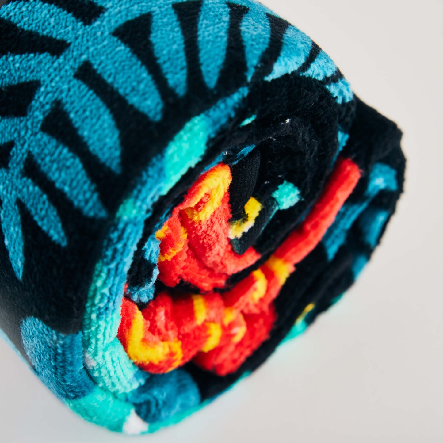 A close-up of the rolled Guinness x Fatti Burke Hawaiian Beach Towel, featuring blue, black, orange, and red patterns inspired by Hawaii, set against a light background.