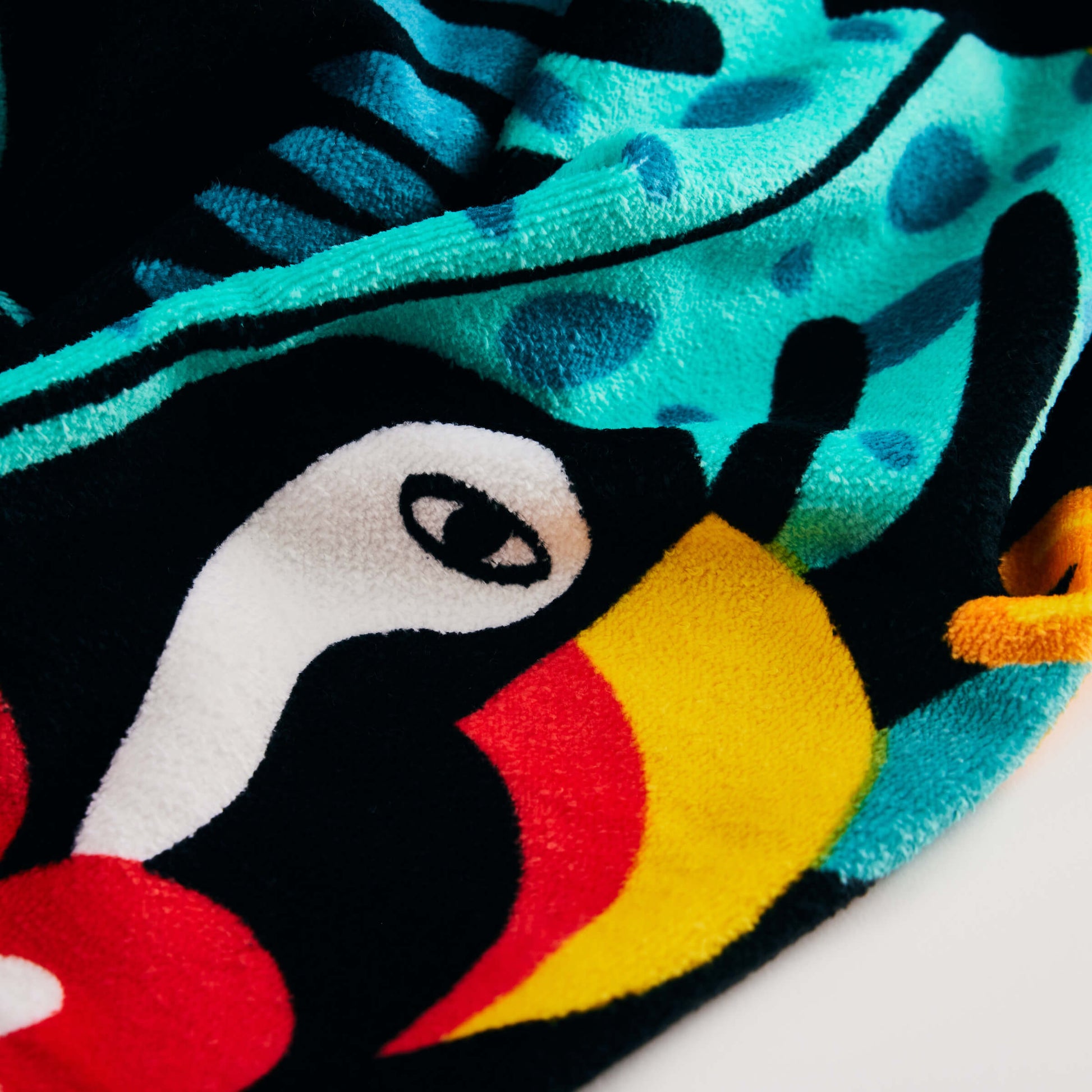 A close-up of the Guinness x Fatti Burke Hawaiian Beach Towel by Guinness, showcasing vibrant abstract shapes and patterns in black, white, teal, yellow, red, and blue—evoking the lively look of a colorful fleece fabric.