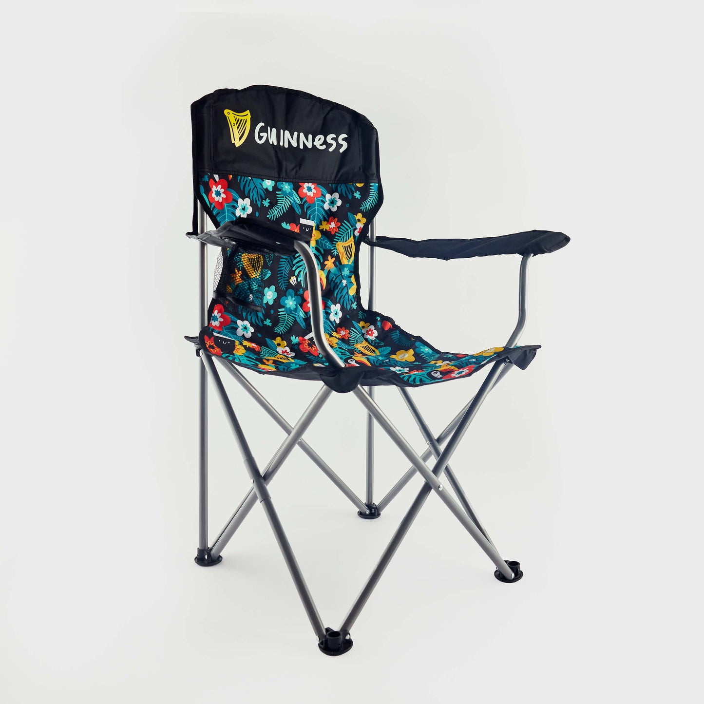 The Guinness x Fatti Burke Hawaiian Camping Chair features metal legs, black armrests, vibrant floral fabric like a Hawaiian beach towel, and a "Guinness" logo on the backrest.