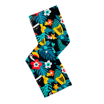 Bring a lively island vibe to your beach or poolside experience with the Guinness x Fatti Burke Beach Day Bundle from Guinness Webstore US—a rectangular fabric towel adorned with a colorful tropical pattern of leaves, flowers, toucans, and monkeys on a black background.