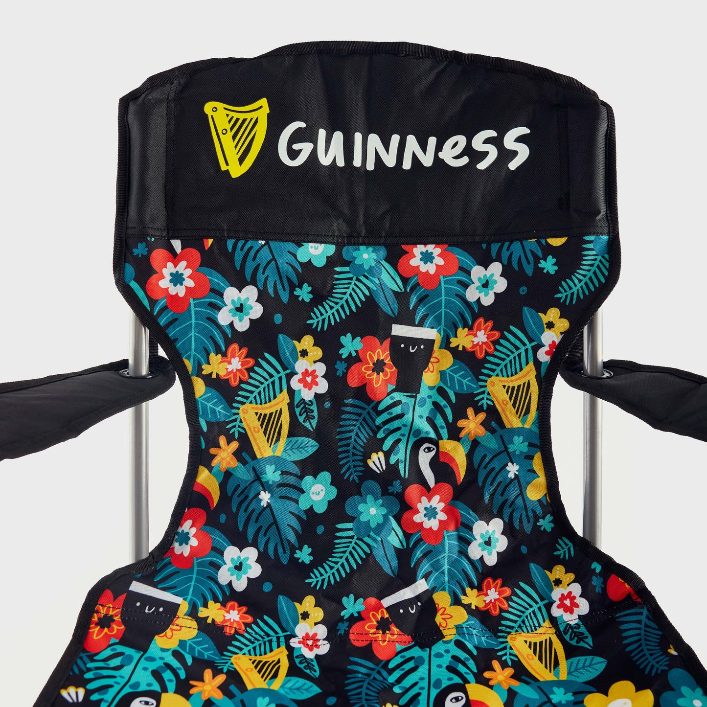 The Guinness x Fatti Burke Hawaiian Camping Chair by Guinness features a black fabric backrest with the "Guinness" logo and a vibrant seat adorned with tropical flowers and toucans, reminiscent of a Hawaiian beach towel.