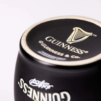 Close-up of a Guinness branded glass with a logo featuring a harp and the text "ESTD 1759 GUINNESS & CO.," akin to the charming design on the Guinness Toucan Black Mini Barrel Mug from Guinness Webstore US.