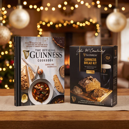 The Guinness Baking Gift Set from Guinness Webstore US, with a cookbook and bread kit, is displayed on a wooden table with holiday lights softly blurred in the background.