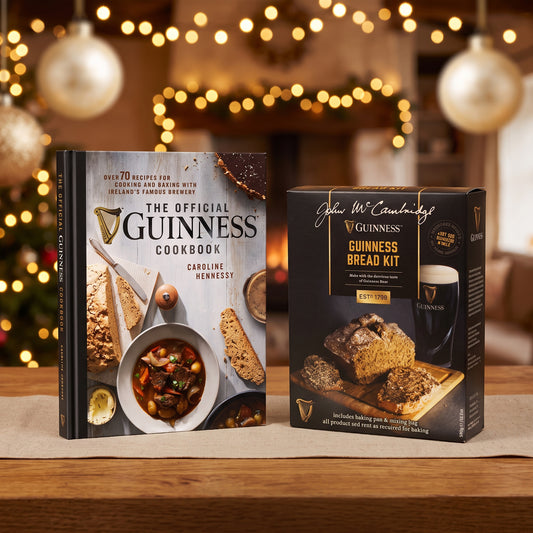 The Guinness Baking Gift Set from Guinness Webstore US, with a cookbook and bread kit, is displayed on a wooden table with holiday lights softly blurred in the background.