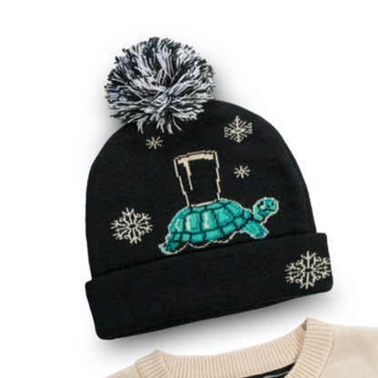 The Guinness Webstore US offers a black and beige sweater paired with the Guinness Holiday Tortoise Beanie, which showcases a black and cream tortoise carrying a pint on its back, accented with snowflakes and featuring "Guinness" on the sleeve. It's an ideal addition to your winter wardrobe.