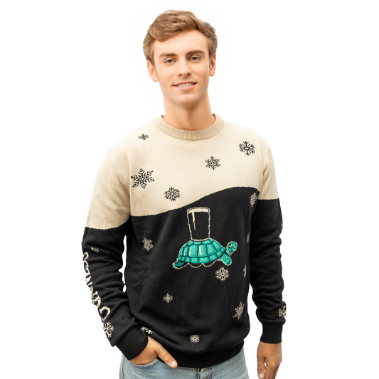 A young man wears the Guinness Holiday Black and Cream Tortoise Sweater from the Guinness Webstore US, featuring snowflake patterns and a turtle carrying a pint glass, against a white background.