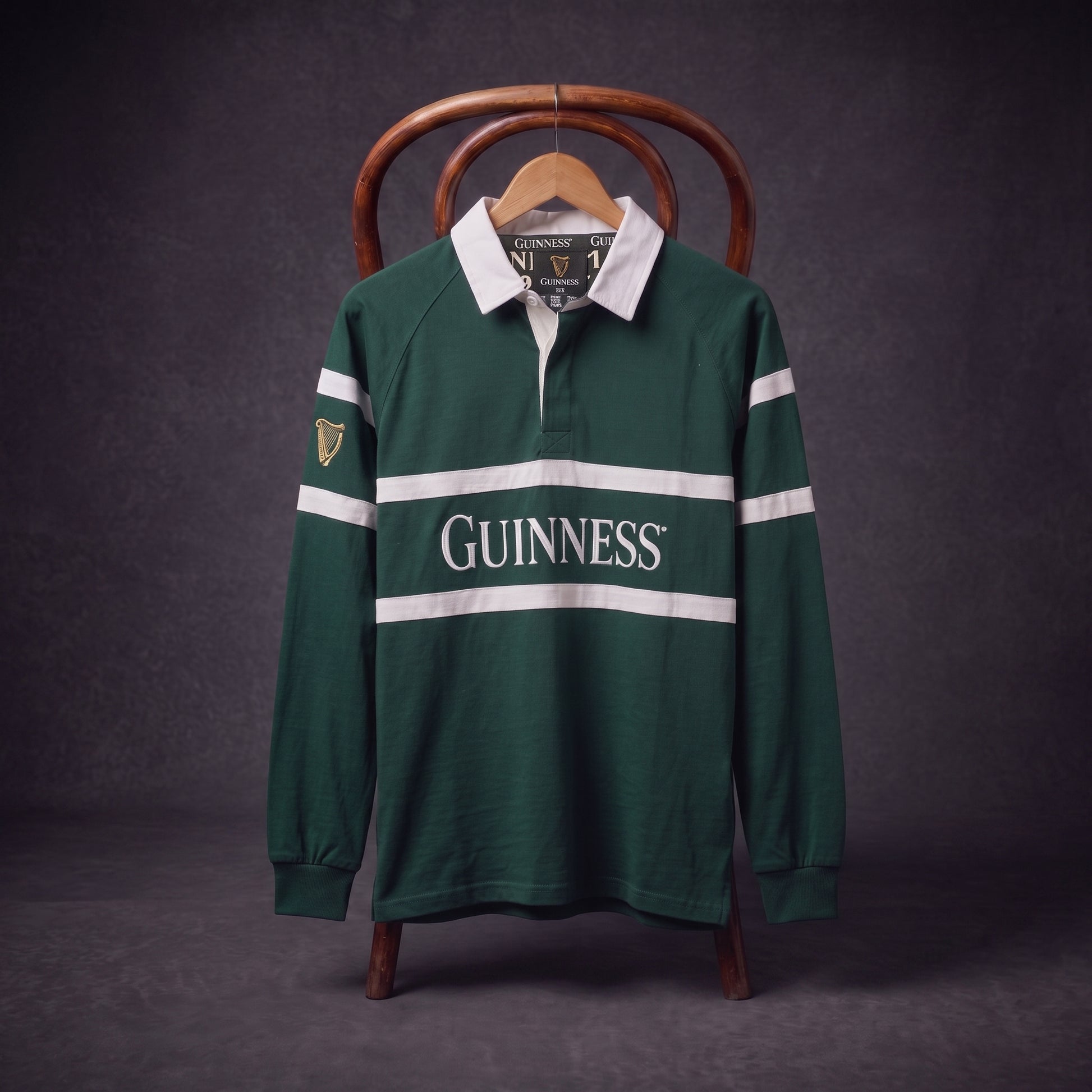 A Guinness Green Traditional Rugby Jersey with white stripes and “Guinness” printed on the front hangs on a wooden chair against a dark background.