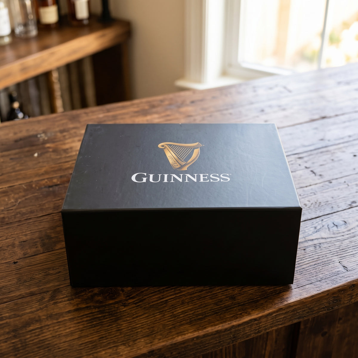 A black Guinness Gift Box - Large with the Guinness logo printed in gold on the lid, resting on a wooden table.