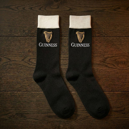 Guinness Pint Crew Socks – Black, featuring the iconic logo and harp, make an ideal Guinness gift, stylishly displayed on a wooden surface.