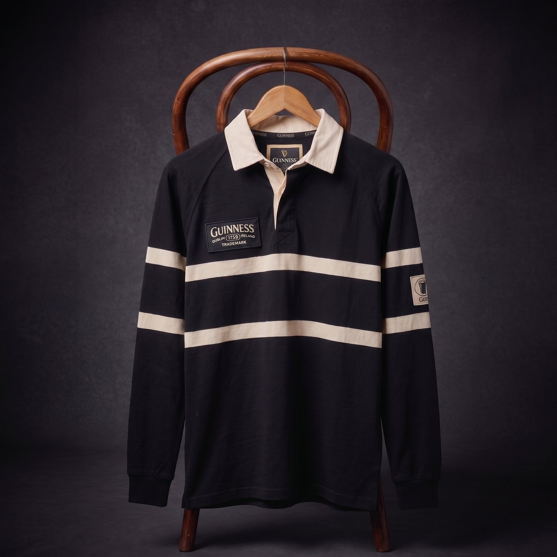 The Guinness Black Traditional Rugby Jersey, featuring classic white stripes and bold Guinness branding, hangs on a wooden hanger against a dark background. Made from 100% cotton, this long-sleeve jersey blends iconic style with comfortable craftsmanship.