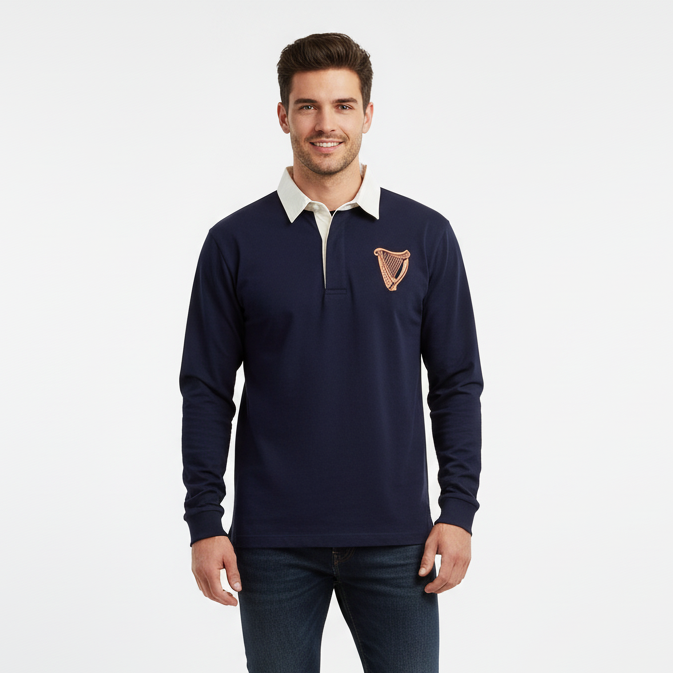 A man models the Guinness Navy Long Sleeve Rugby Shirt – 100% Cotton Vintage Style Top by Guinness Webstore US, featuring a tan collar and embroidered harp emblem, against a white background and radiating classic Irish style.