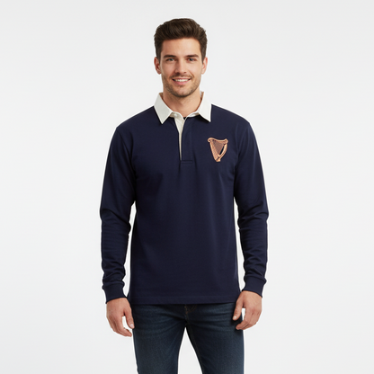 A man models the Guinness Navy Long Sleeve Rugby Shirt – 100% Cotton Vintage Style Top by Guinness Webstore US, featuring a tan collar and embroidered harp emblem, against a white background and radiating classic Irish style.