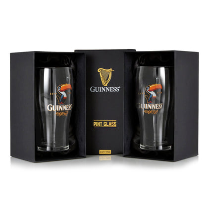 The Guinness Toucan Pint Glass Twin Pack includes two pint glasses with the classic Toucan Graphic, presented in black boxes. The central box reads "Guinness Pint Glass," reflecting the brand's iconic advertising style.