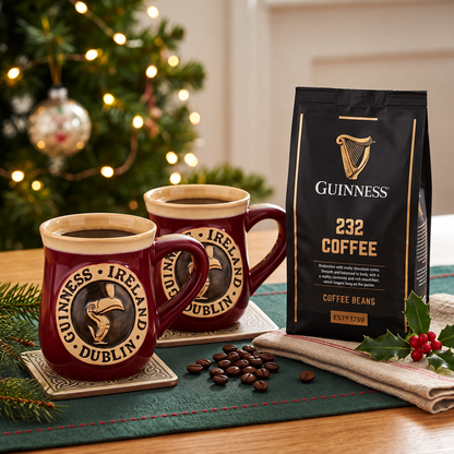 Two mugs of coffee sit beside a Guinness Morning Gift Set from Guinness Webstore US, with a Christmas tree and festive decorations in the background.