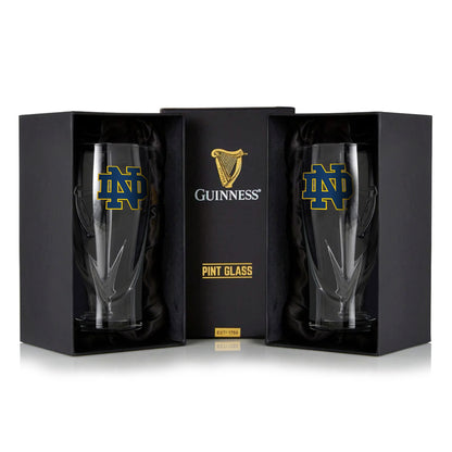 The Guinness Notre Dame 16oz Pint Glass Twin Pack features two elegant pint glasses in black packaging, each with the iconic Notre Dame logo in blue and gold, paired with classic Guinness branding.