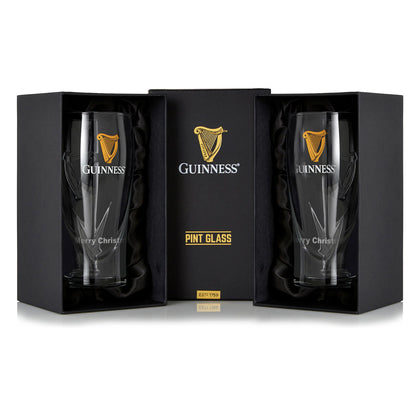 The Guinness Pint Glass Twin Pack features two glasses with an embossed logo, elegantly presented in black packaging. "Merry Christmas" adorns the glasses, making them an ideal festive gift.