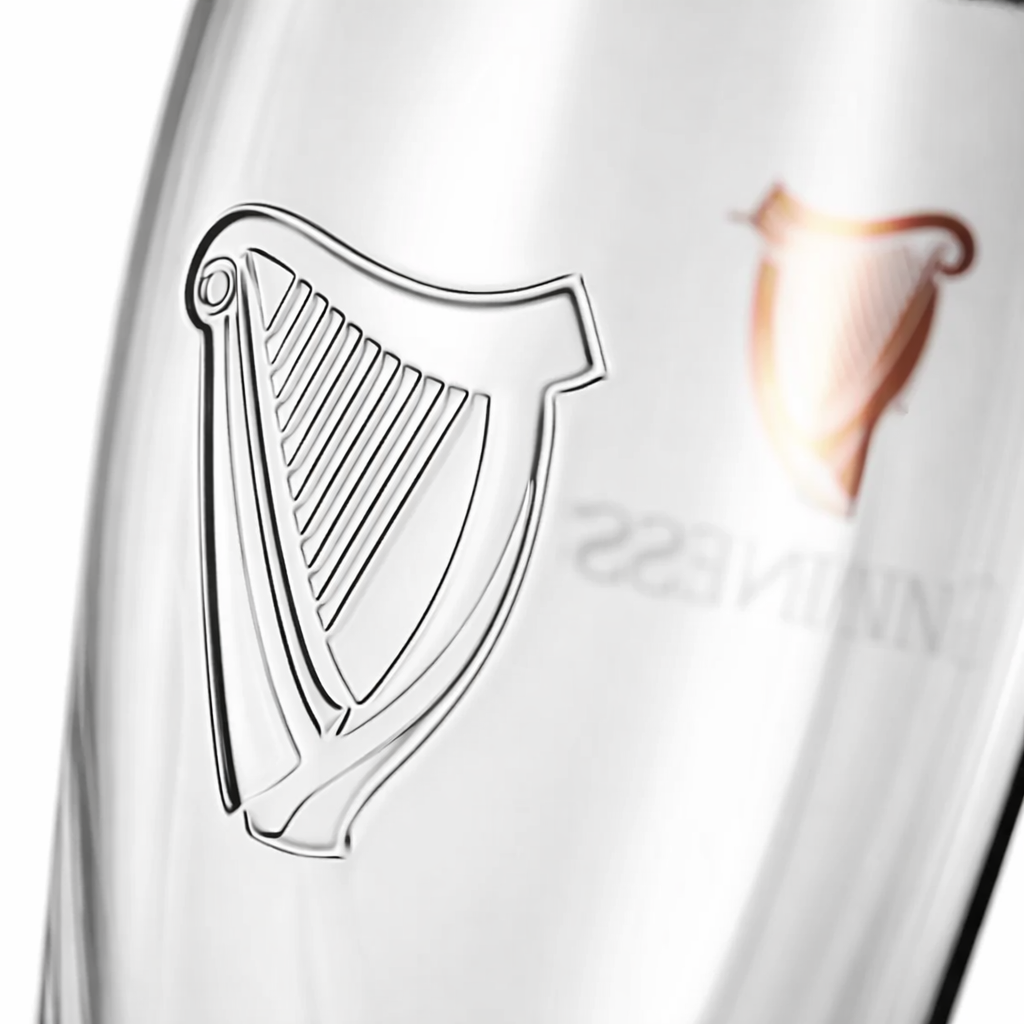 Close-up of a Guinness Pint Glass by Guinness, showcasing an embossed harp design and a partial reflection of the "Guinness" logo.