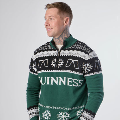 A man wearing the Guinness Holiday Quarter Zip Sweater in green, featuring black accents, white snowflake patterns, and “GUINNESS” across the front; a festive Irish Christmas jumper from Guinness, perfect for the holiday season.