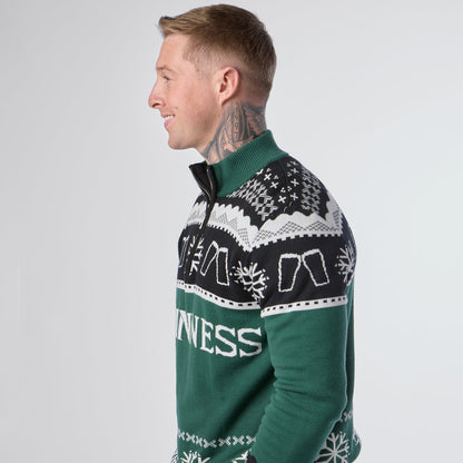 A man with neck tattoos is standing sideways and smiling against a plain background while wearing the Guinness Holiday Quarter Zip Sweater in green, featuring black and white patterns and festive text from the Guinness brand.