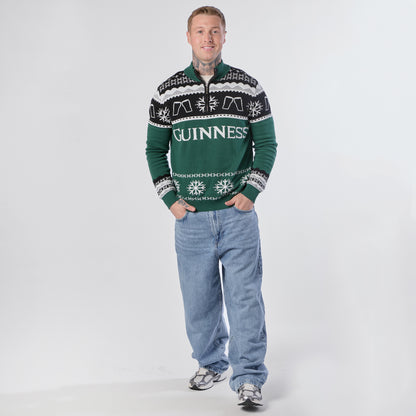 A person stands facing forward, wearing the Guinness Holiday Quarter Zip Sweater in green and black from Guinness, paired with blue jeans and sneakers, against a plain white background.
