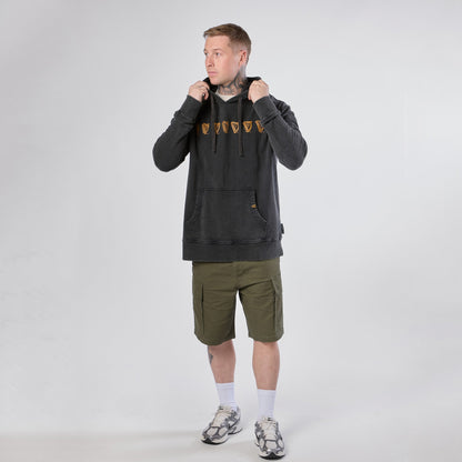 A person wearing a Guinness Evolution of the Harp Distressed Hoodie – Black from Guinness Webstore US, paired with olive green cargo shorts, white socks, and sneakers, stands against a plain white background while holding the hoodie’s drawstrings.