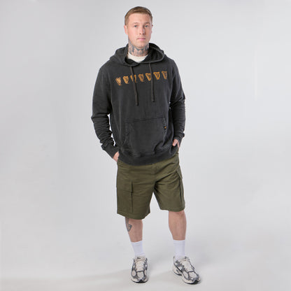 A person stands facing forward against a plain light background, wearing the Guinness Evolution of the Harp Distressed Hoodie in black from Guinness Webstore US, paired with olive cargo shorts, white socks, and gray sneakers.