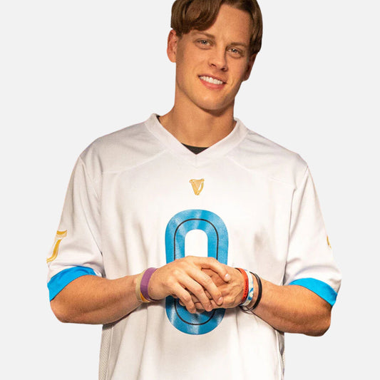 A man stands smiling with his hands clasped, proudly wearing the Guinness 0 Football Jersey - White from Guinness Webstore US, featuring a bold blue number 0 on the front.