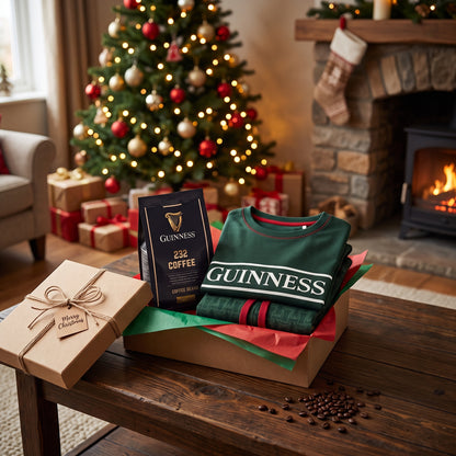 A Guinness Christmas Morning Gift Set containing a bag of coffee beans and a folded green sweater in a box on a wooden table, with a Christmas tree and fireplace in the background.