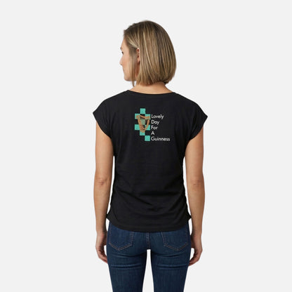 A woman faces away, wearing the Guinness Toucan Ruched Ladies Black Tee from Guinness Webstore US, which features a toucan graphic and "Lovely Day For A Guinness" text on the back.