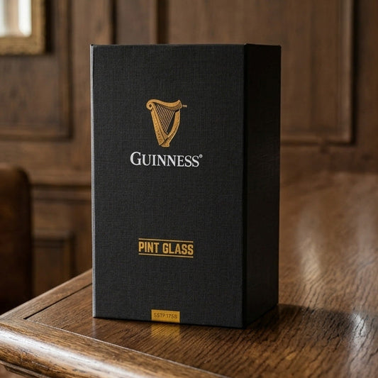 A black rectangular Guinness Gift Box - Pint Glass with gold text, sitting on a wooden table.