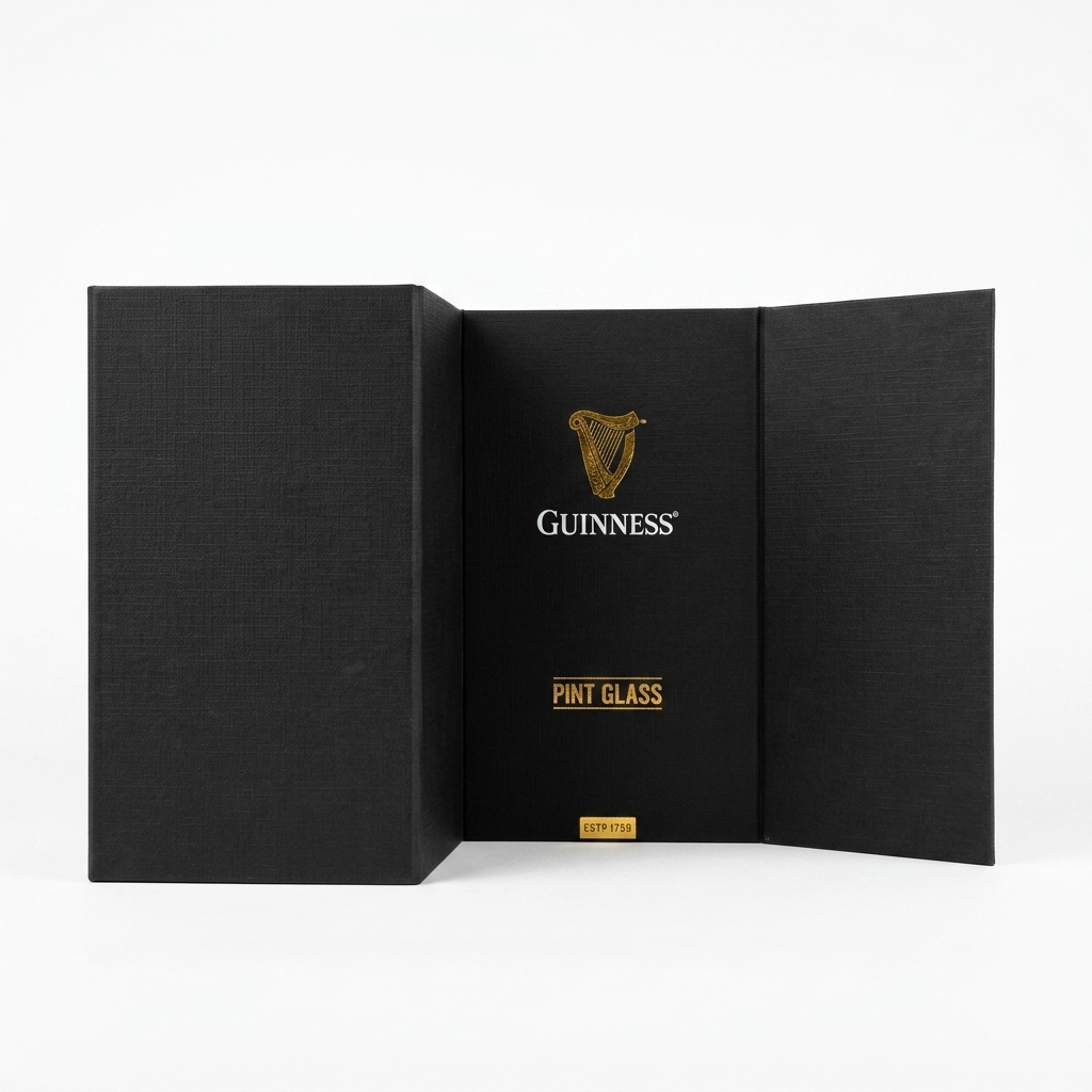 A black box with open side panels displays the Guinness Pint Glass Luxury Gift Box from Guinness Webstore US, showcasing the words “Pint Glass” and a bold gold Guinness harp logo at the center, all set against a crisp white background.