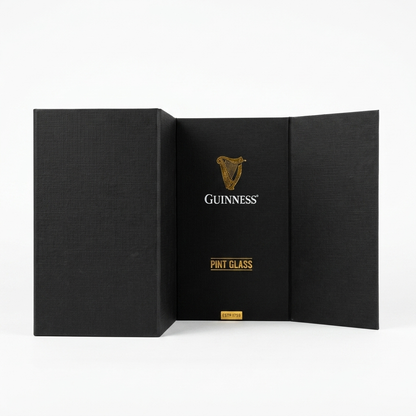 A black box with open side panels displays the Guinness Pint Glass Luxury Gift Box from Guinness Webstore US, showcasing the words “Pint Glass” and a bold gold Guinness harp logo at the center, all set against a crisp white background.