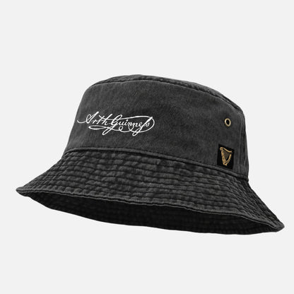 The Guinness Signature Bucket Hat is a black hat with white "Arthur Guinness" cursive text signature and a gold harp logo patch on the side—an ideal gift for any Guinness fan.