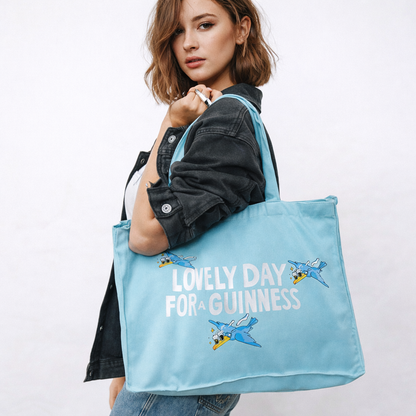 A woman carries the Guinness Summer Collection Tote Bag - Blue from Guinness Webstore US, featuring "Lovely Day For A Guinness" and playful flying toucans on the front.