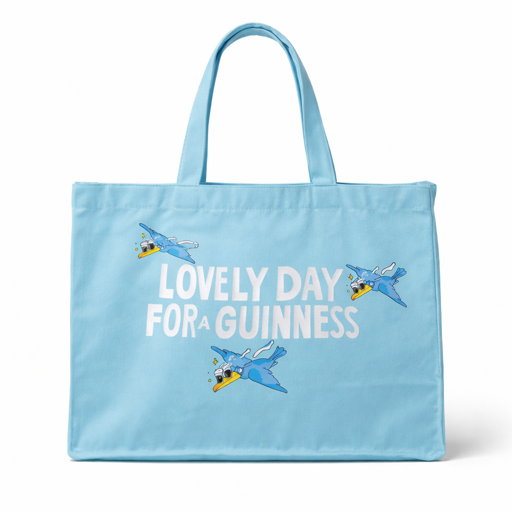 The Guinness Summer Collection Tote Bag - Blue from Guinness Webstore US is an oversized light blue cotton bag featuring “Lovely Day For A Guinness” and three cartoon toucans flying above and around the text.