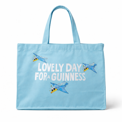 The Guinness Summer Collection Tote Bag - Blue from Guinness Webstore US is an oversized light blue cotton bag featuring “Lovely Day For A Guinness” and three cartoon toucans flying above and around the text.