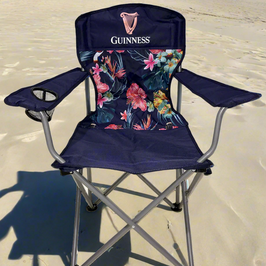 The Guinness Toucan Hawaiian Beach Chair from the Guinness Webstore US showcases a blue floral design with the "Guinness" logo, armrests, and a cup holder. It's an ideal match for the Guinness Toucan Hawaiian Cooler Bag on your outdoor adventures.