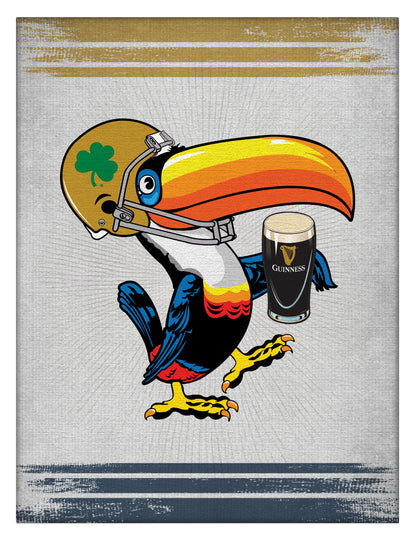 Guinness Notre Dame Toucan Canvas Wall Art by Guinness features a cartoon toucan in a football helmet with a shamrock, holding a pint of Guinness, on gray with gold and blue borders—ideal decor for any fan’s space.