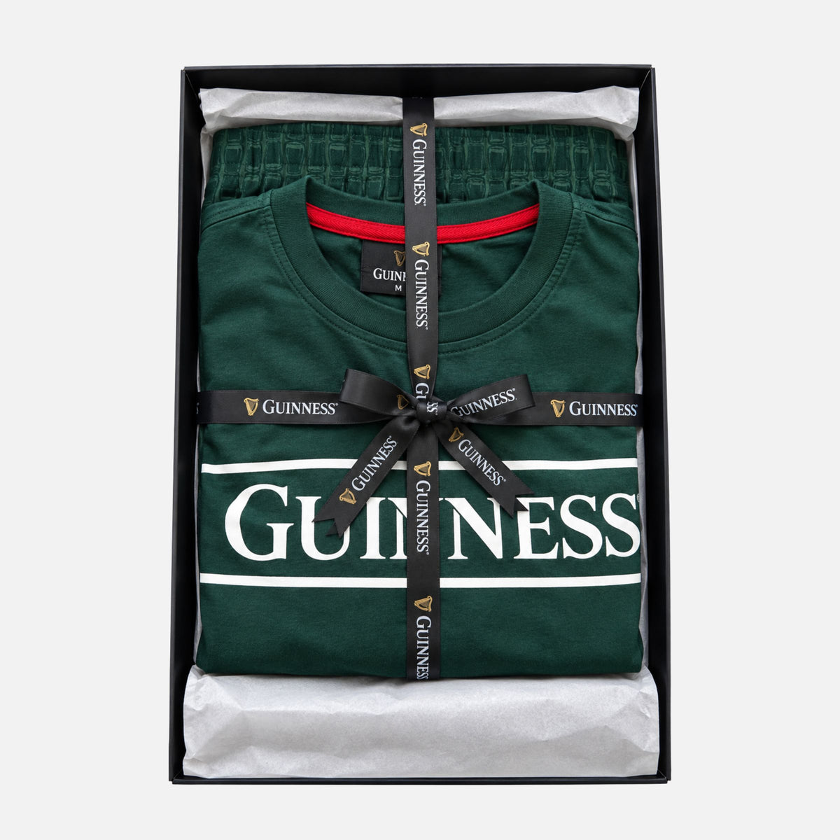 Guinness Unisex 2-Piece Pajama Set – Green featuring a graphic logo shirt and matching pants, folded in a gift box and tied with a branded ribbon.