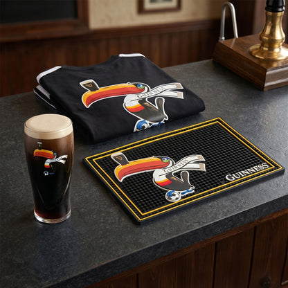 The Guinness Soccer Matchday Premium Pack from Guinness Webstore US, including a pint of Guinness, Soccer Pint Glass, and bar mat with the toucan logo, is displayed on a pub countertop.