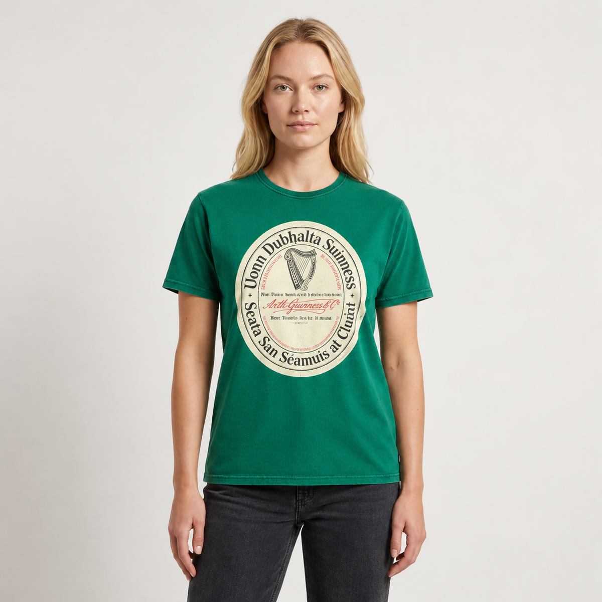 A person wearing a Guinness Green Label Premium Tee, a green crew-neck t-shirt featuring a circular logo with a harp illustration and Irish text.