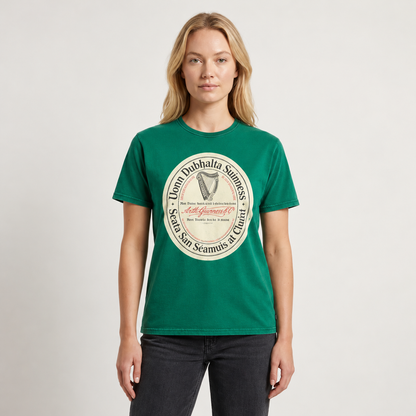A person wearing a Guinness Green Label Premium Tee, a green crew-neck t-shirt featuring a circular logo with a harp illustration and Irish text.